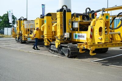 Rij gele Mobix gerailde machines op een werfterrein met een Mobix-medewerker in geel t-shirt
