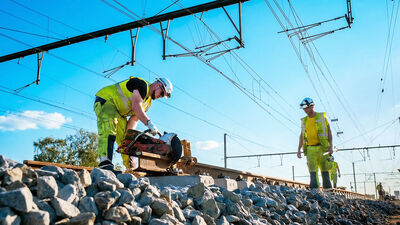 Twee Mobix spoorwerkers in gele hi-vis kleding aan het werk op het spoor onder de bovenleiding