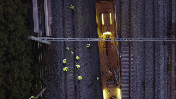 Luchtfoto van Mobix spoorwerkers in gele hi-vis kleding bij een gele werkwagon op de spoorlijn